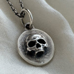 Silver necklace with a skull pendant on a light fabric background