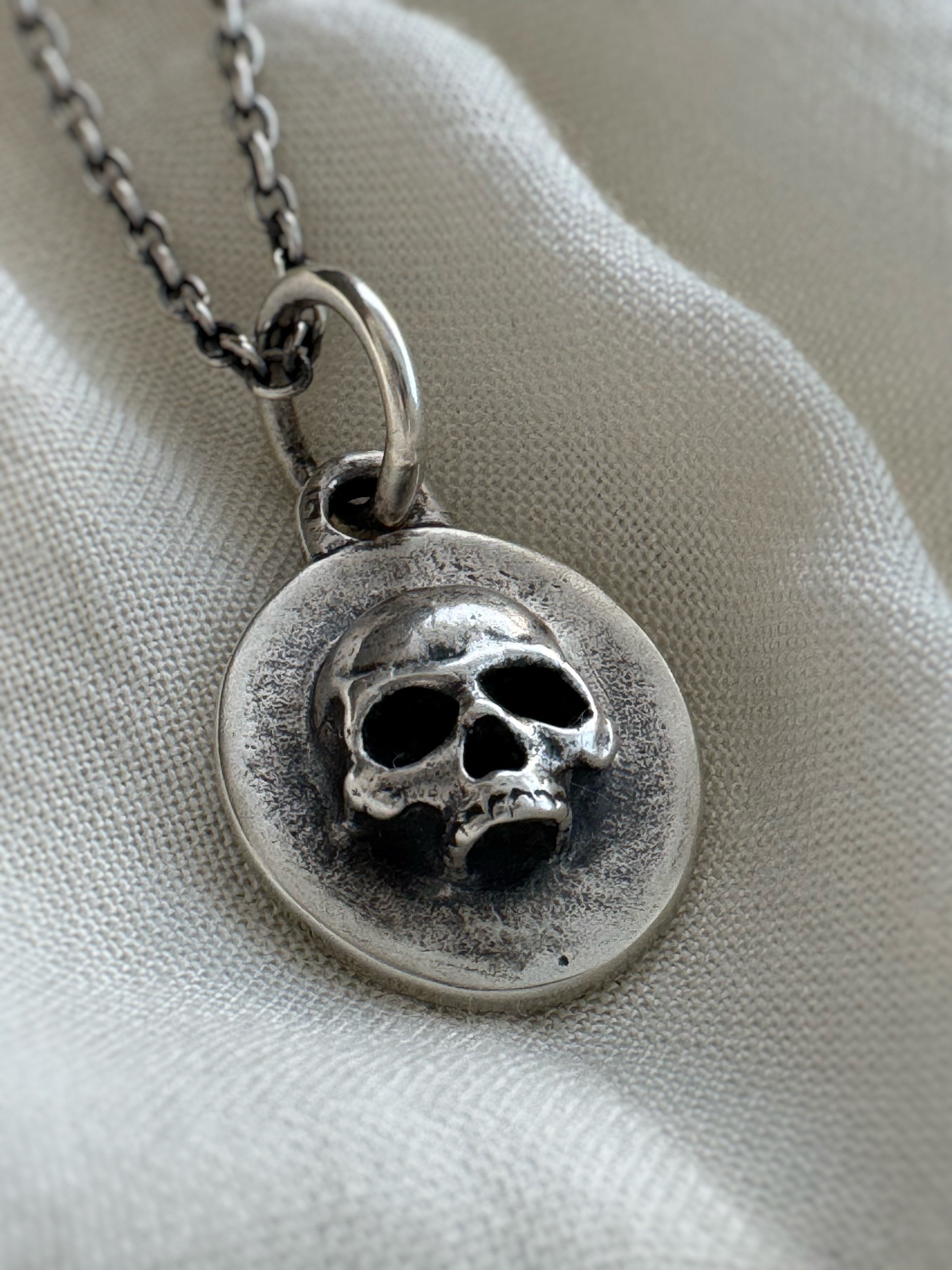 Silver necklace with a skull pendant on a light fabric background