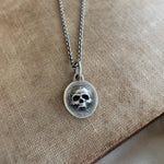 Silver necklace with a skull pendant on a beige fabric background