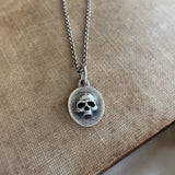 Silver necklace with a skull pendant on a beige fabric background