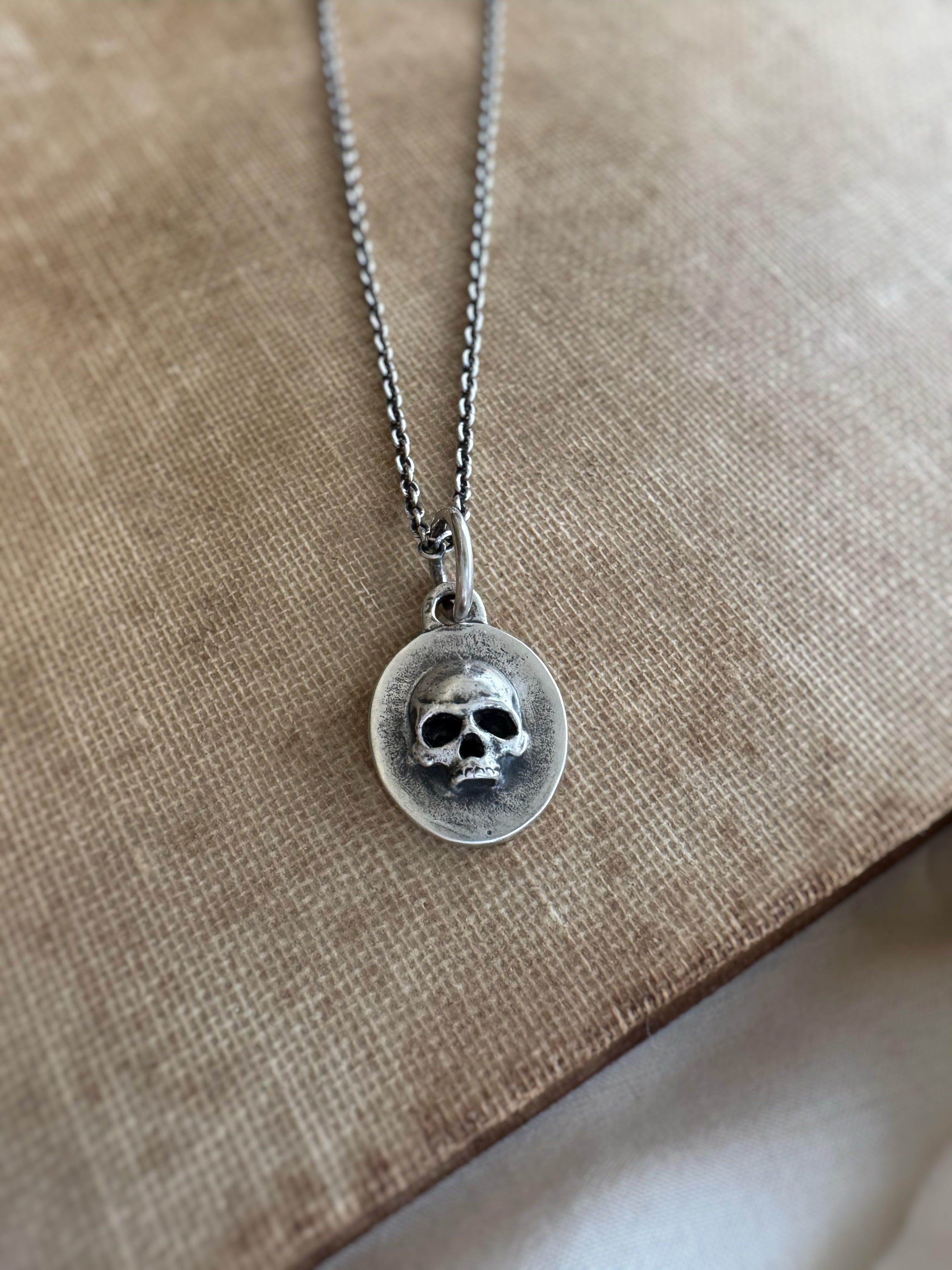 Silver necklace with a skull pendant on a beige fabric background
