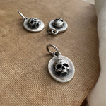 Silver skull pendant and earrings on a textured surface