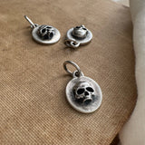 Silver skull pendant and earrings on a textured surface