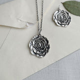 Silver rose necklace and charm on a light gray background