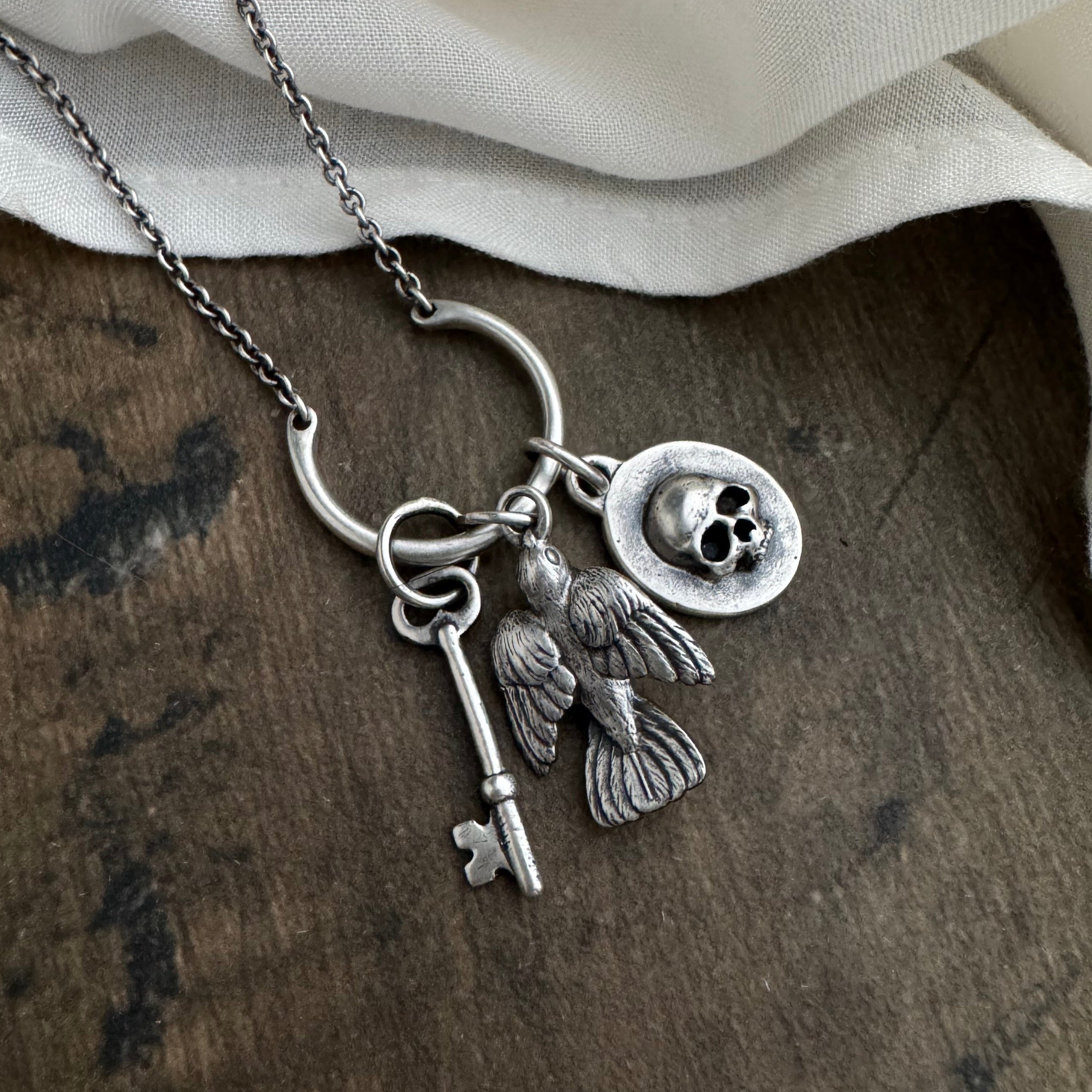 Silver necklace with key, sparrow, and skull charm on a wooden surface