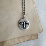 Silver necklace with a bird pendant on a beige paper background