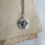 Silver necklace with a bird pendant on a beige paper background