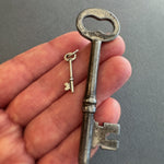 Hand holding a vintage key and sterling silver key charm against a gray background