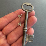 Hand holding a vintage key and sterling silver key charm against a gray background