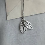 Silver necklace with two pendants on a gray surface with an envelope in the background