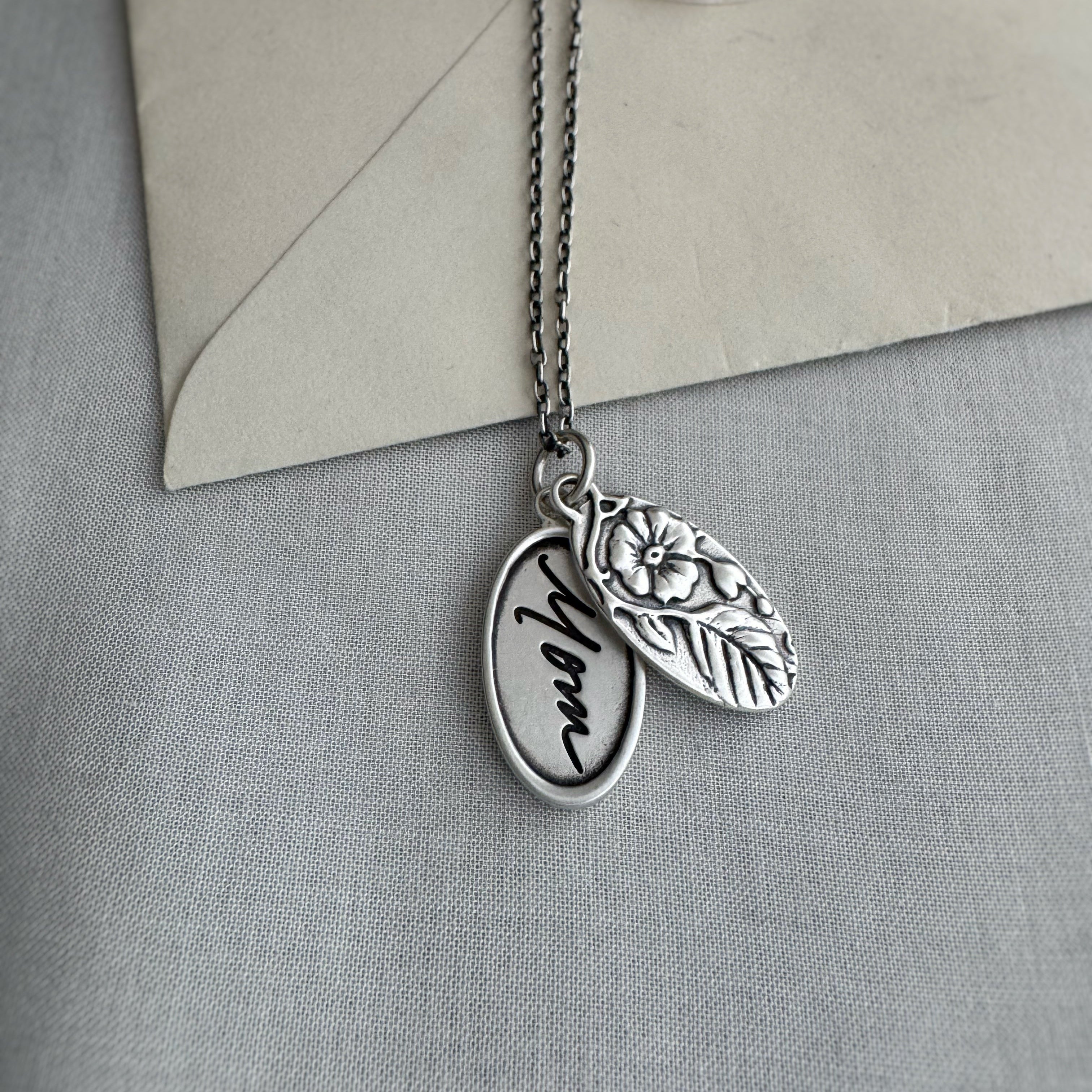 Silver necklace with two pendants on a gray surface with an envelope in the background