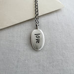 Silver necklace with 'love' pendant on a light gray surface