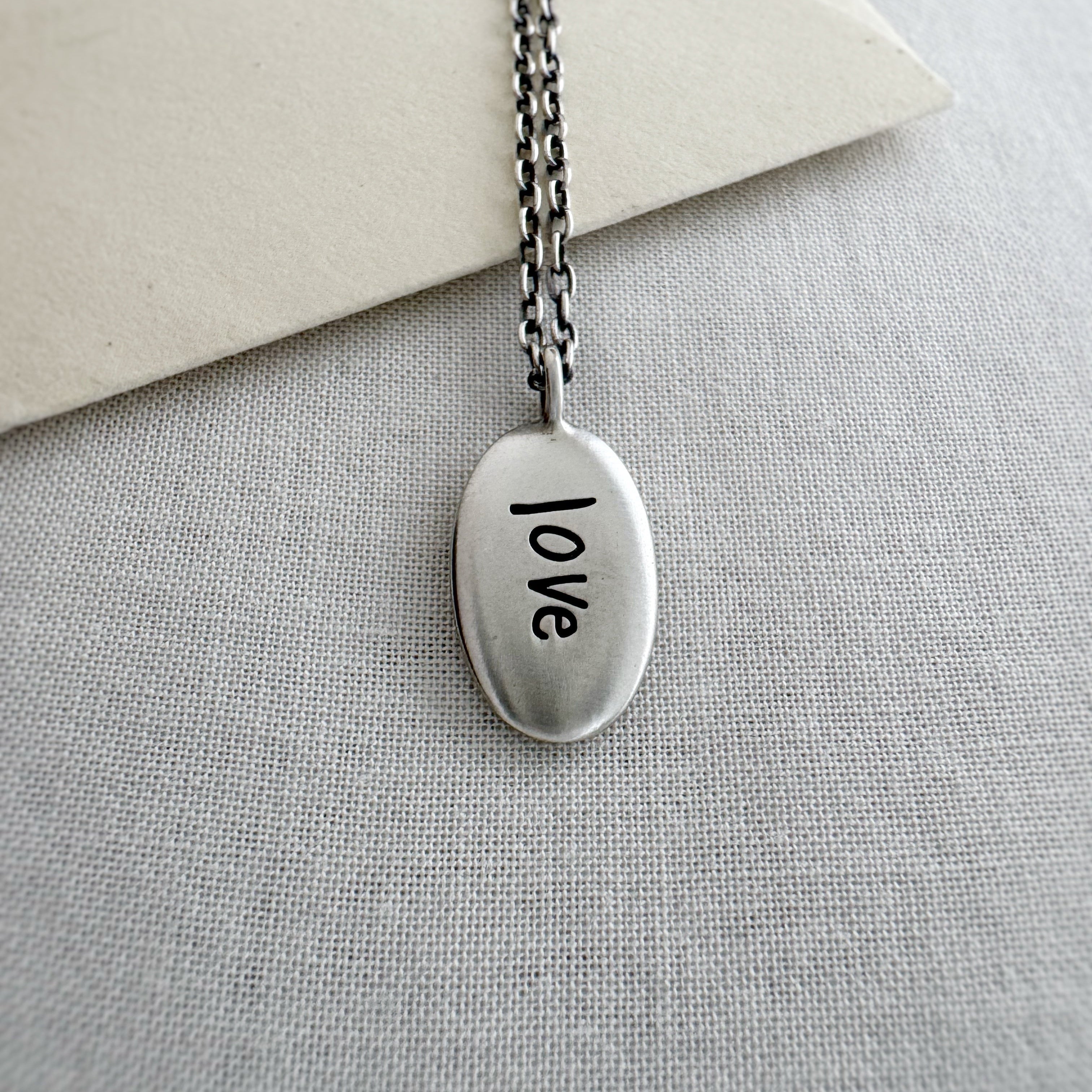 Silver necklace with 'love' pendant on a light gray surface