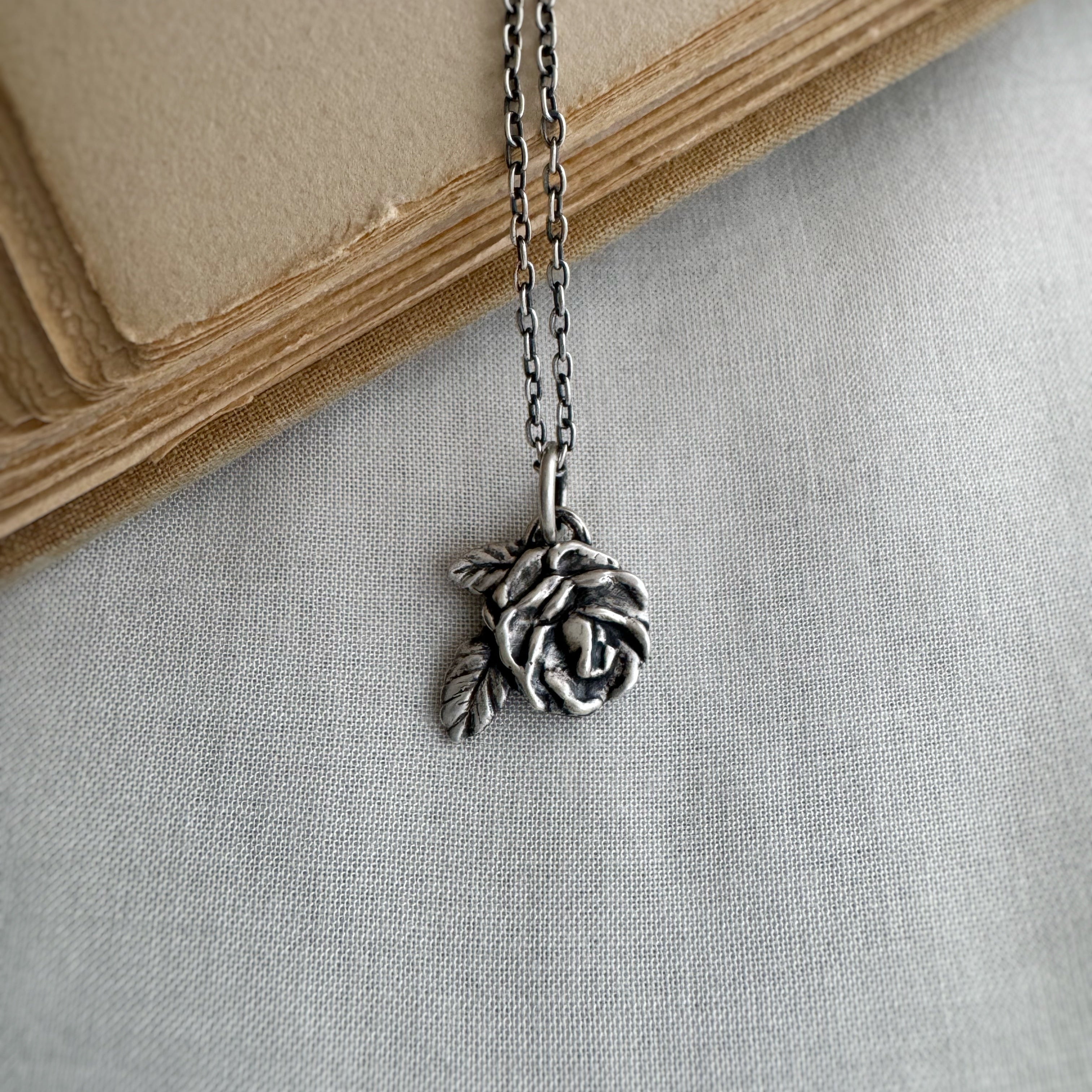 Silver rose necklace on a light gray fabric background