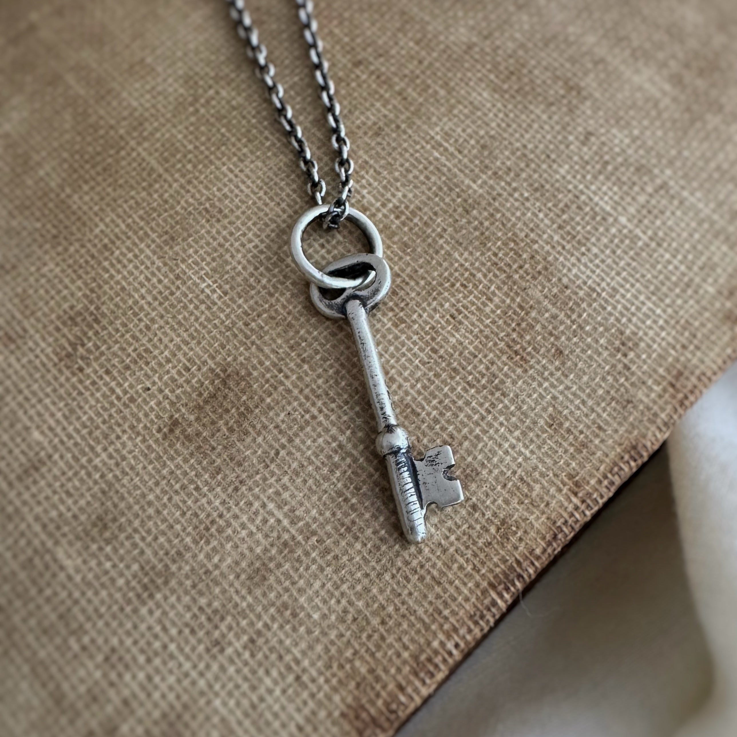 Silver key necklace on a textured beige surface