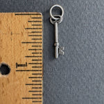Small silver key charm next to a wooden ruler on a gray background. Key measures 3/4" long