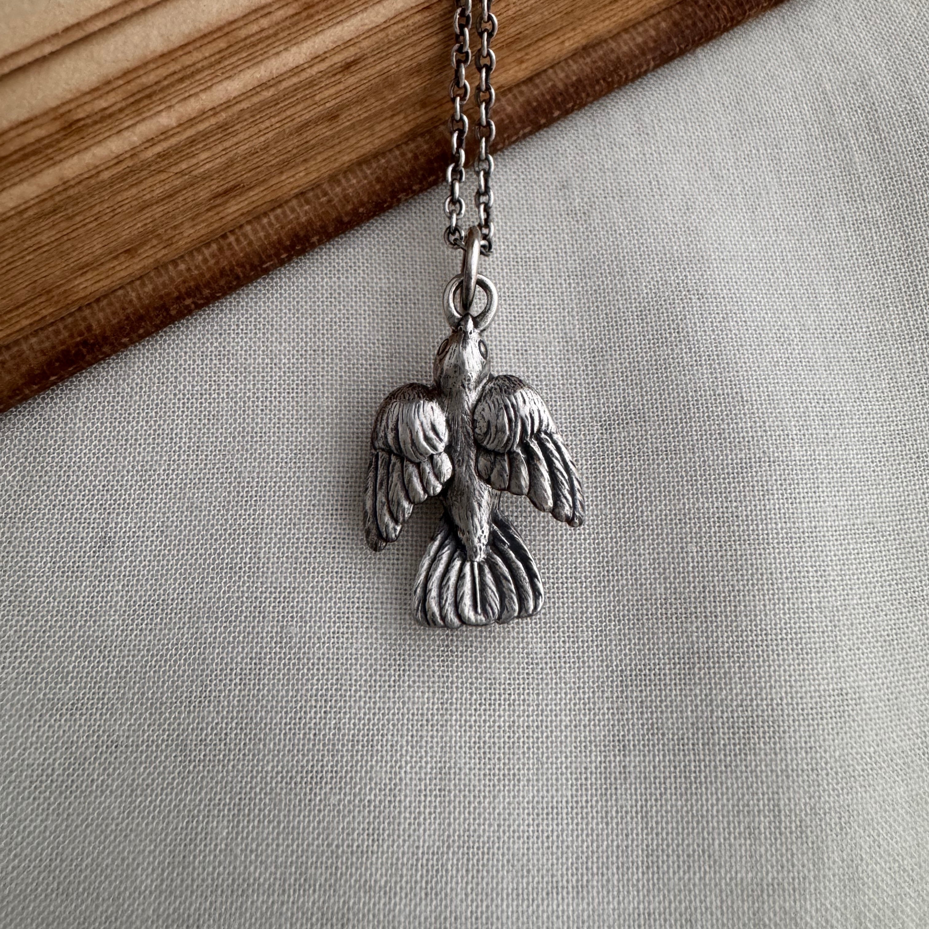 Sterling silver sparrow charm necklace. A hand sculpted bird pendant hangs on a chain against a neutral background