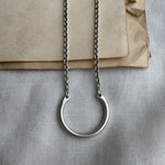 Silver necklace with a circular pendant on a textured surface