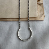 Silver necklace with a circular pendant on a textured surface
