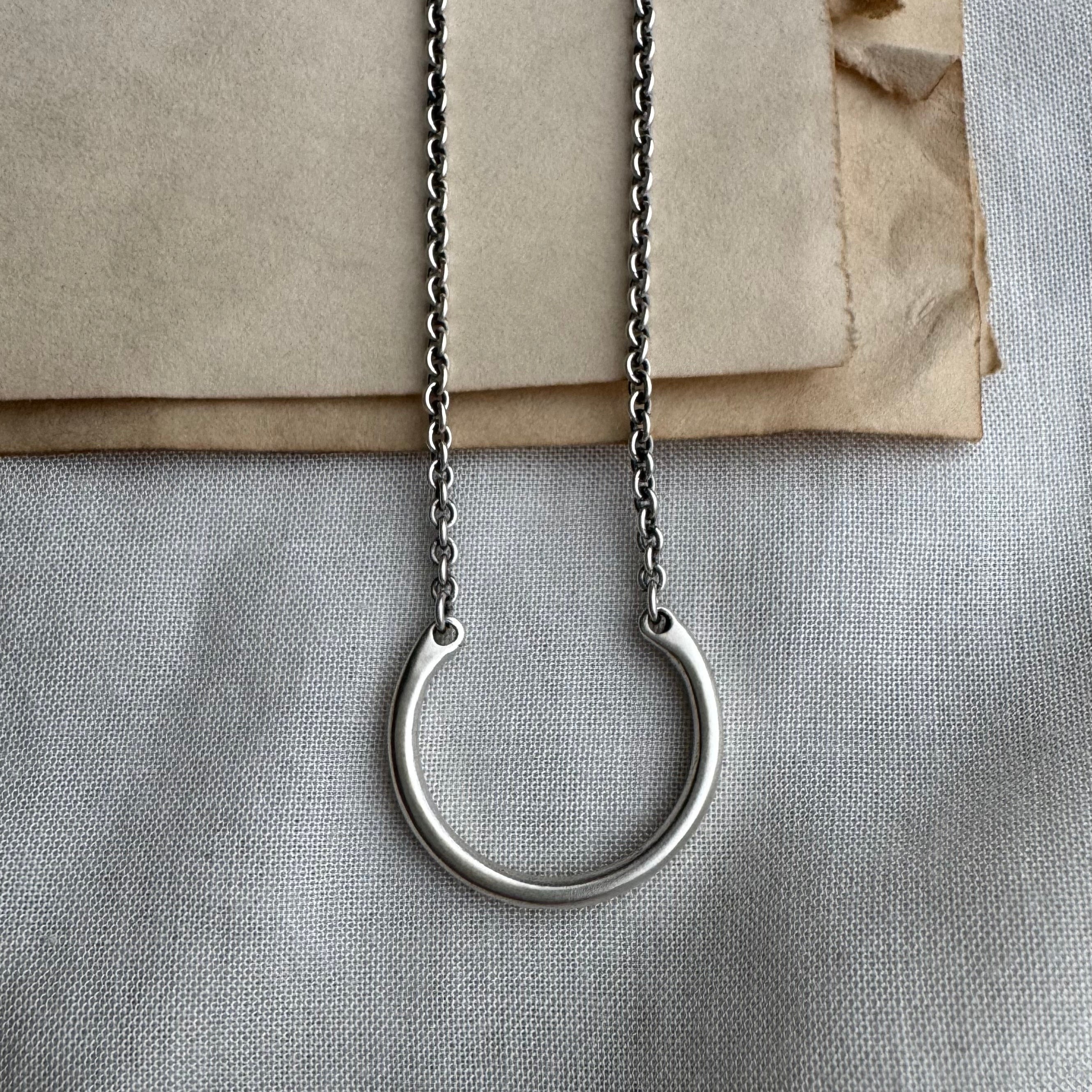 Silver necklace with a circular pendant on a textured surface