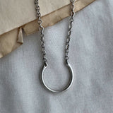 Silver necklace with a circular pendant on a textured surface