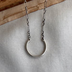 Silver necklace with a large ring pendant on a neutral background