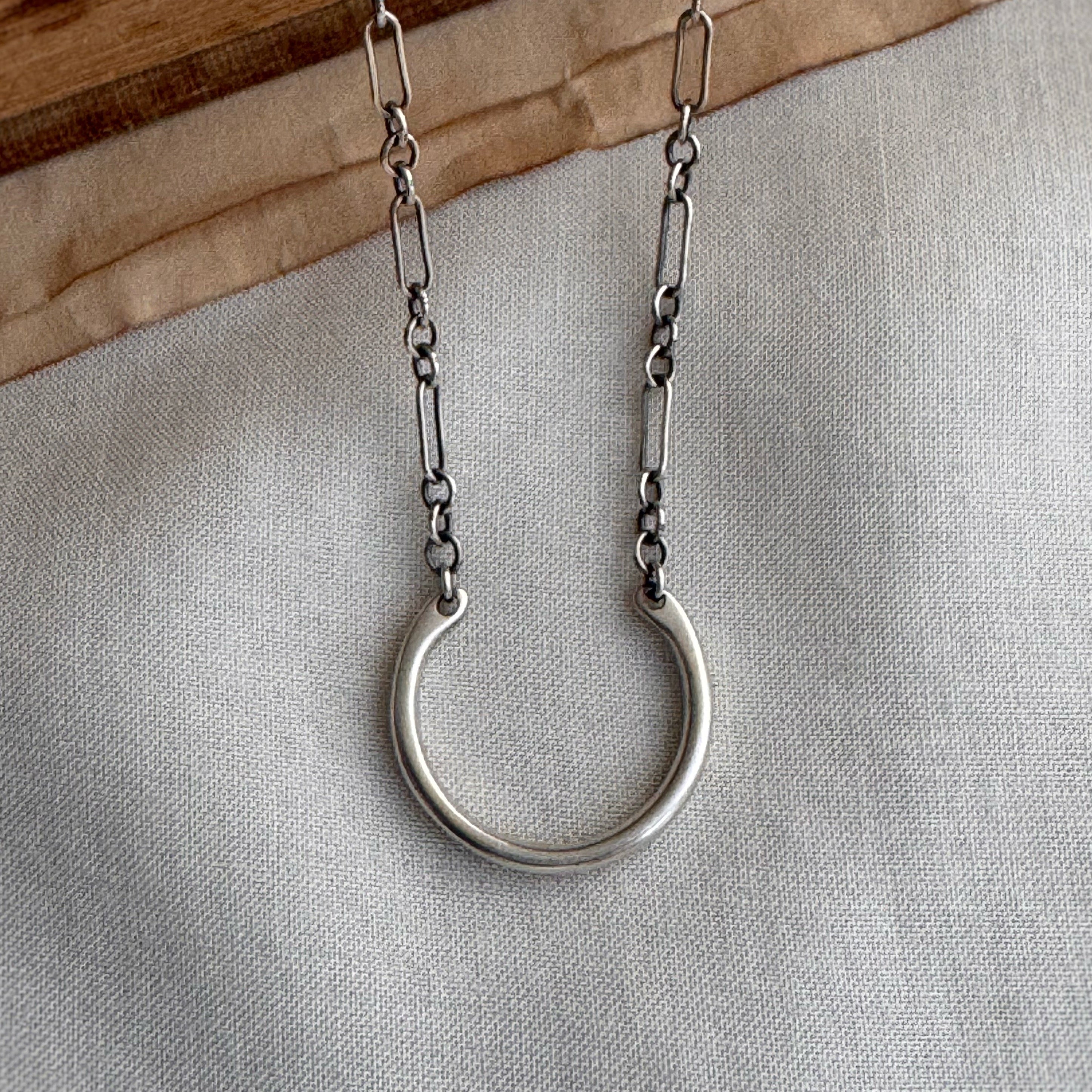 Silver necklace with a large ring pendant on a neutral background