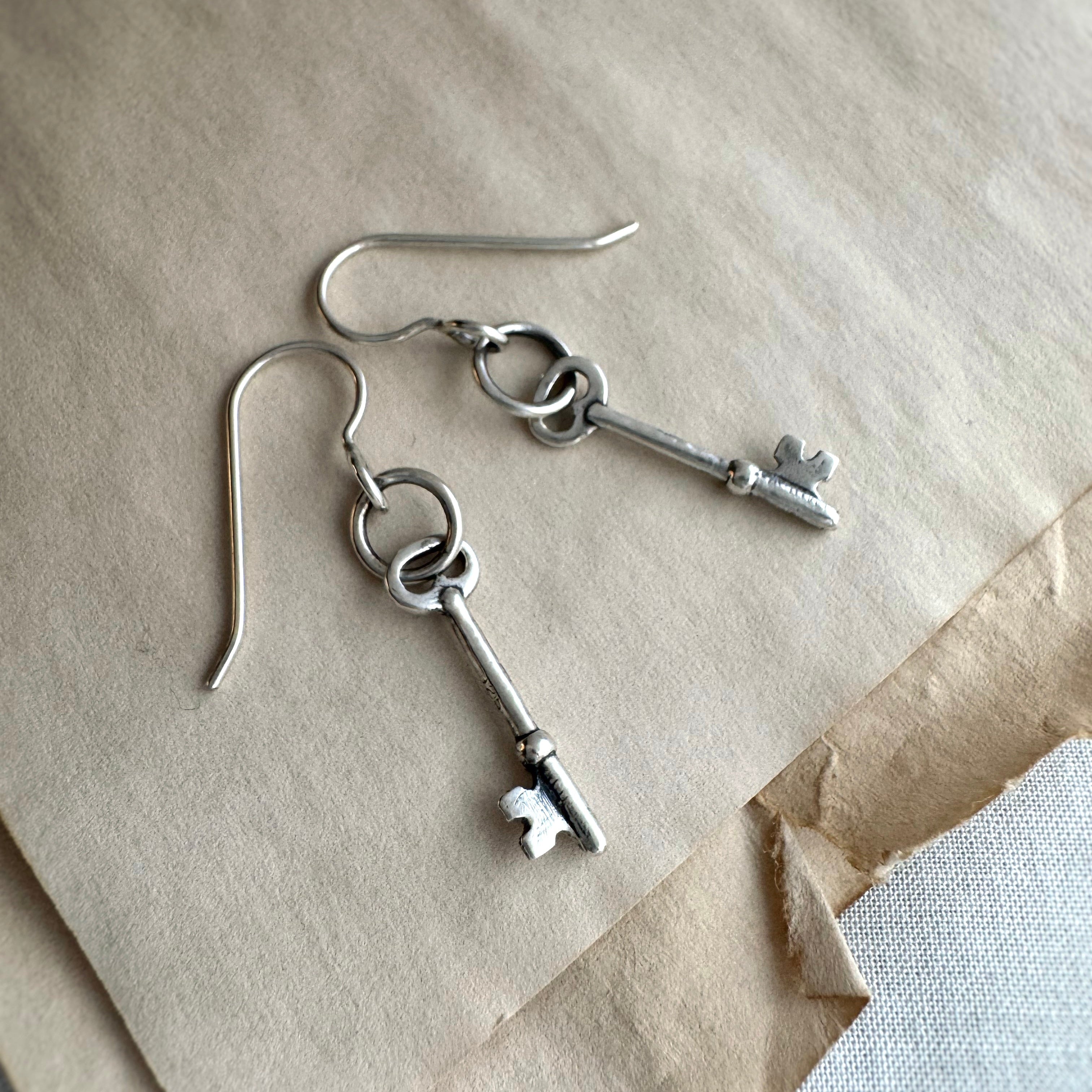 Silver skeleton key earrings on a textured surface