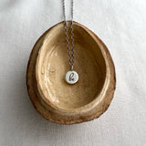 Necklace with a pendant labeled 'be' on a ceramic dish against a light background