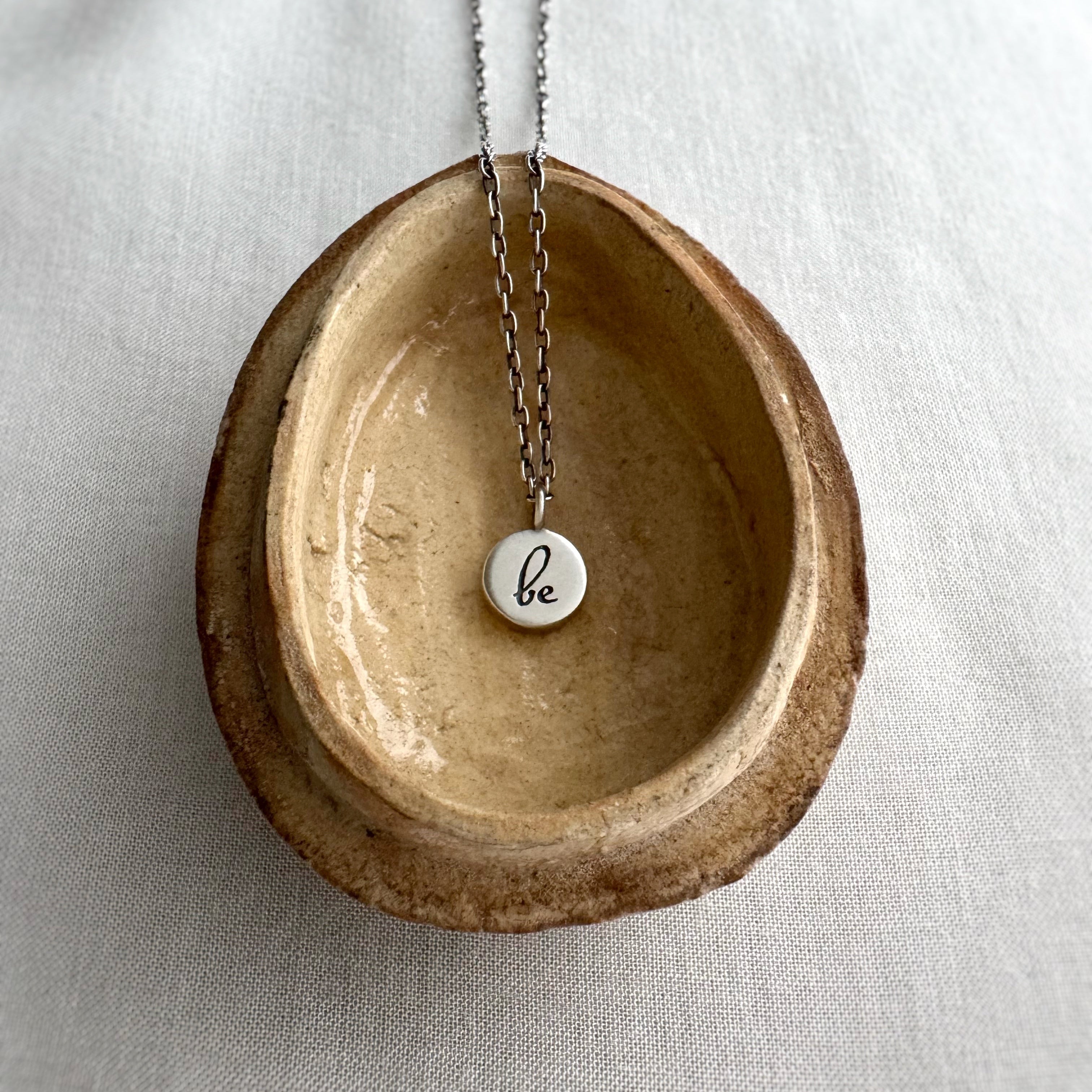 Necklace with a pendant labeled 'be' on a ceramic dish against a light background