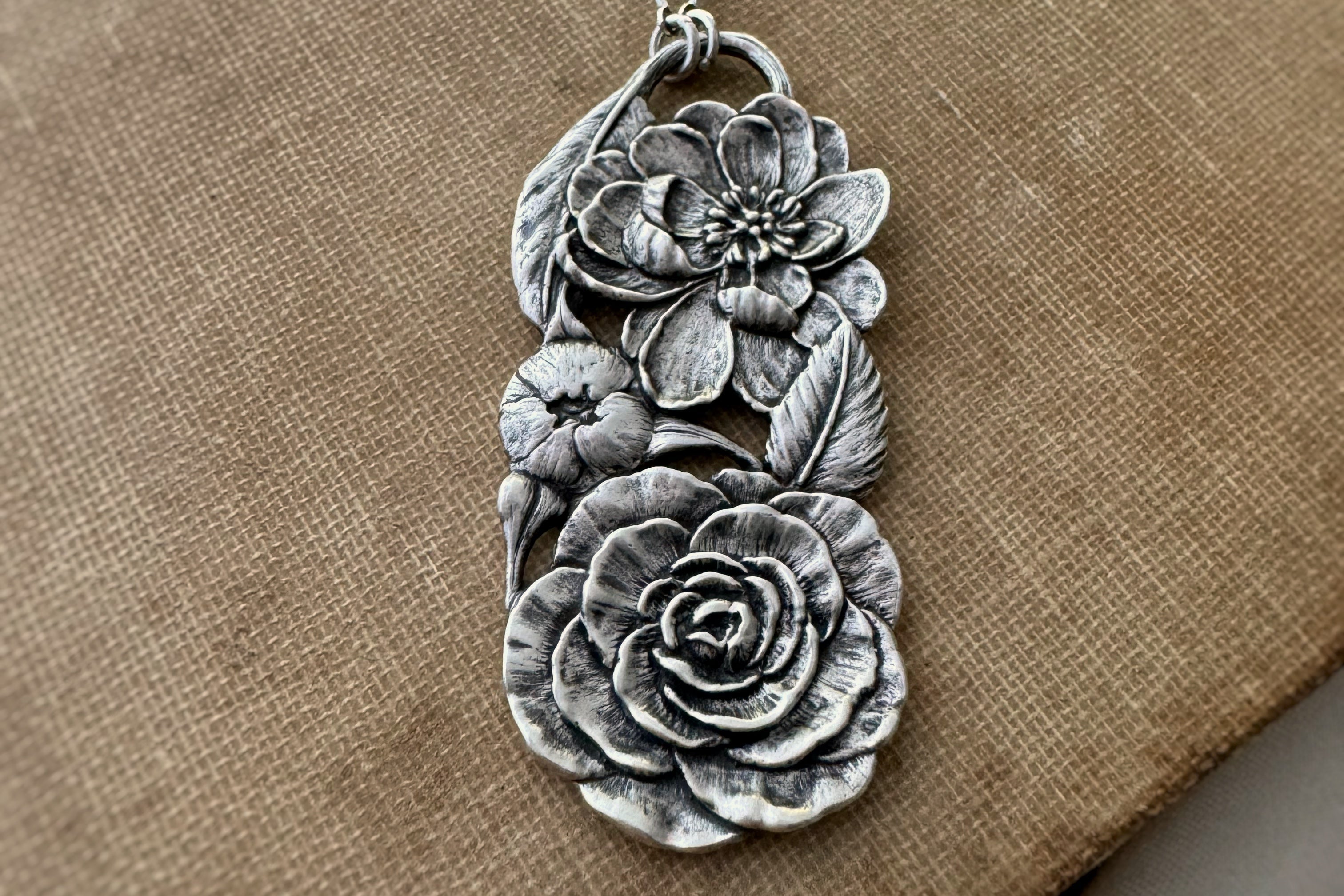 Silver floral pendant on a brown fabric background