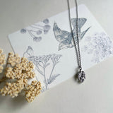Sterling silver sparrow necklace on post card with a sparrow, wild flowers, and a butterfly, with dried yarrow